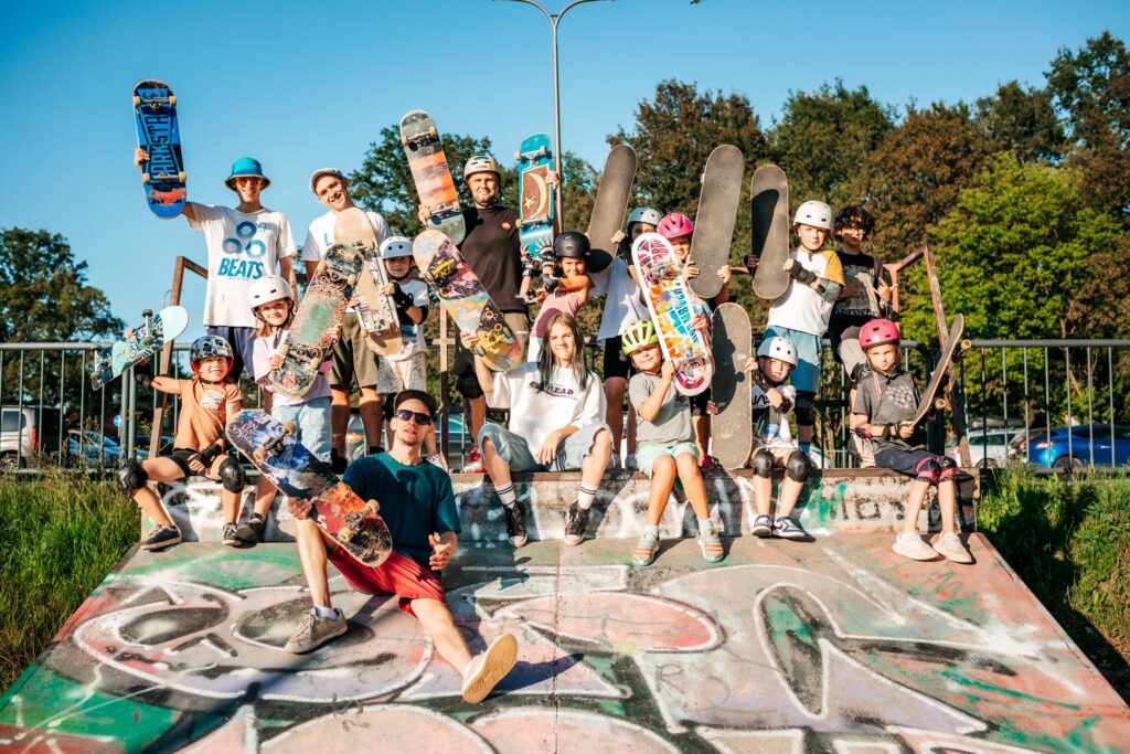 fotografia przedstawia grupę pozującą z deskorolkami do zdjęcia - stoją i siedzą na przeszkodzie na skateparku