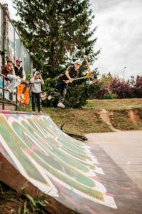 fotografia przedstawia instruktora wykonującego trick na hulajnodze na przeszkodzie na skateparku.