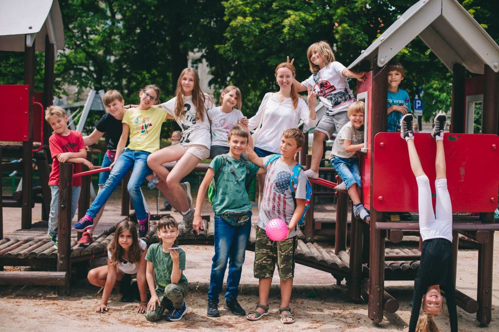 Grupa dzieci w różnym wieku pozuje do zdjęcia na tle placu zabaw.